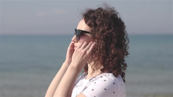 年轻和美丽的女人的特写把耳机在沙滩上听音乐 — 图库视频影像