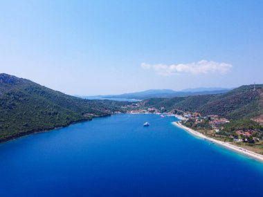 Mavi denizde seyreden lüks bir yat. Etrafı kıyı şeridiyle çevrili. 