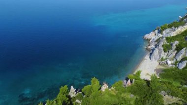 Büyük kayalar ve yeşilliklerle çevrili, açık mavi denizdeki küçük kumsal. Hava görünümü