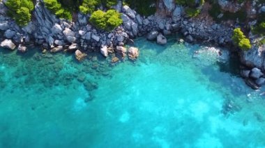 Kayalar ve yeşilliklerle dolu egzotik deniz manzarası ve çeşitli mavi tonlarıyla saydam deniz.