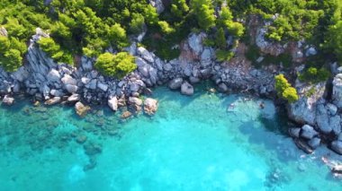 Kayalar ve yeşilliklerle dolu egzotik deniz manzarası ve çeşitli mavi tonlarıyla saydam deniz.