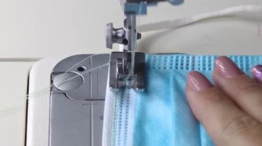 Dikiş makinesinde tıbbi maske takan bir kadın. Covid-19 önleme maskesi dikilüyor