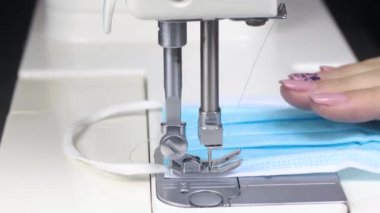 Dikiş makinesinde tıbbi maske takan bir kadın. Covid-19 önleme maskesi dikilüyor