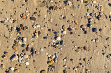Çok renkli küçük taşlar kum kıyıda düz yalan yatıyordu