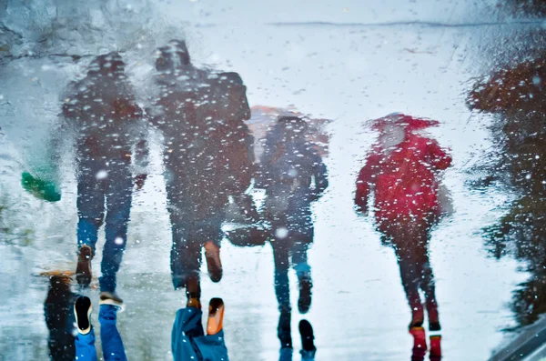 Reflejo borroso en un charco de cuatro personas caminando en la calle de la ciudad húmeda durante la lluvia y la nieve. Concepto de humor —  Fotos de Stock