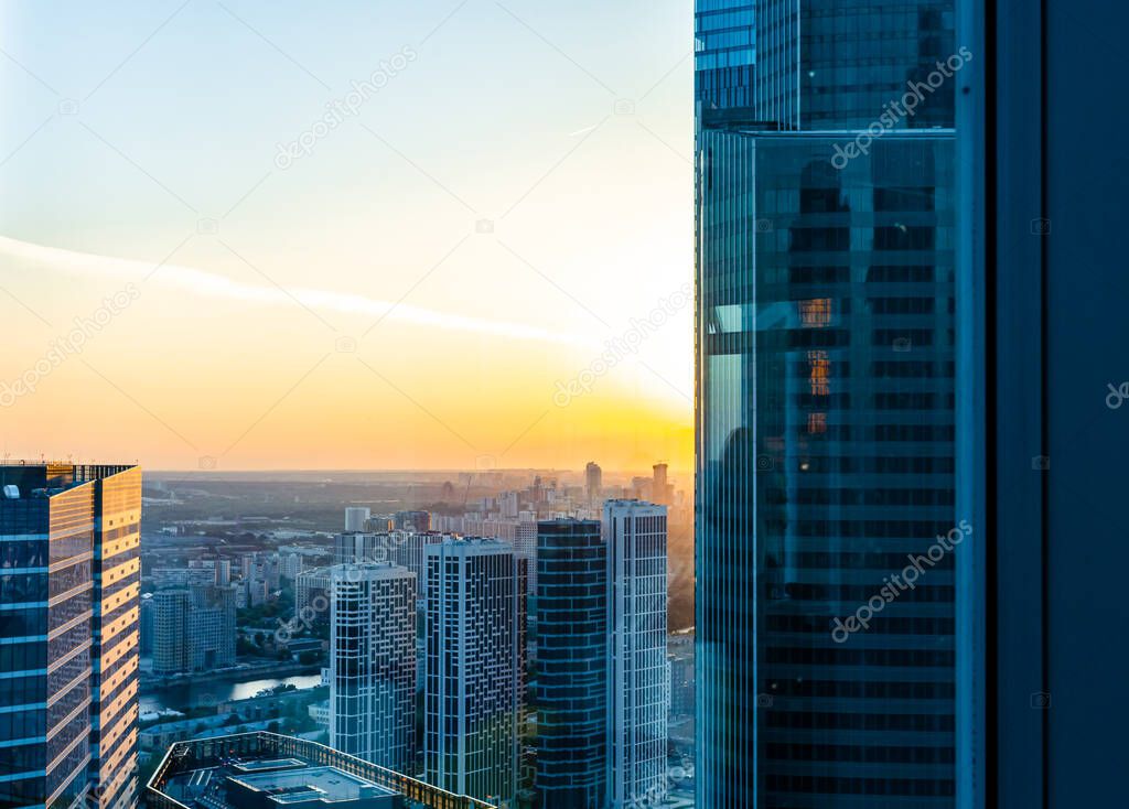 Elevated view of Moscow city business center district looking through the window from high floor. Scenic cityscape with corporate buildings backlit by sunset