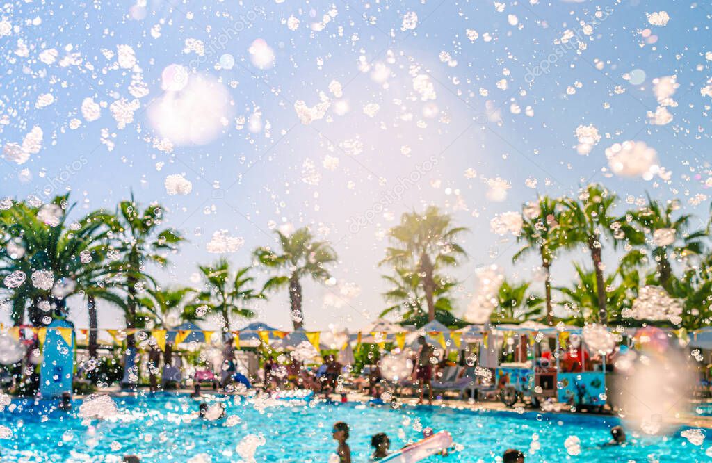 Foam pool party, bubbles blower and pool with people swimmng, dancing, relaxing and having fun against palms background. Summer holidays, fun sports, family travel, tourism