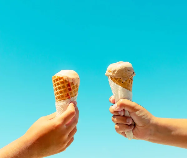 Couple kids hands holding ice cream cones against blue sky background in summer vacation. Summer food, summertime joy, vacation, holidays — Stock Photo, Image