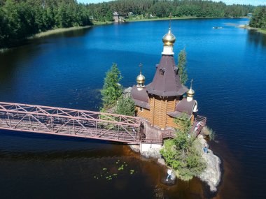 Nehir kıyıları boyunca bir orman ve açık bir yaz gününde ada üzerinde köprüsü olan bir kilise. Vuoksa 'daki St. Andrew Kilisesi. Rusya