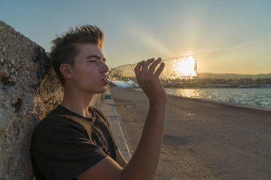 Genç adam içme suyu ile güneşin arkasında şişe,