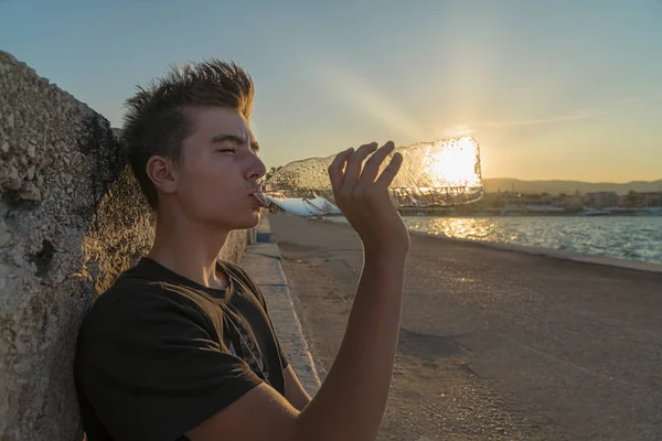 Genç adam içme suyu ile güneşin arkasında şişe,