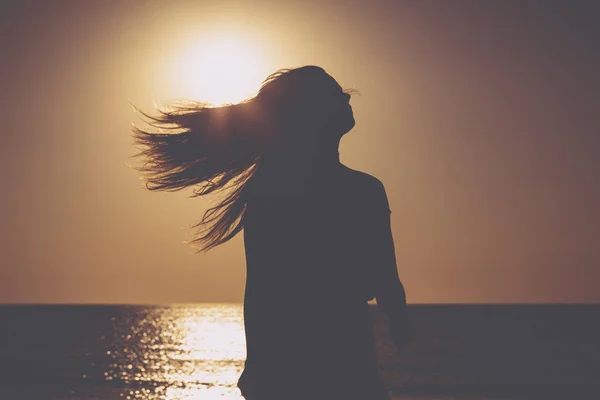 Tramonto su una spiaggia, silhouette di una donna con i capelli volanti — Foto Stock