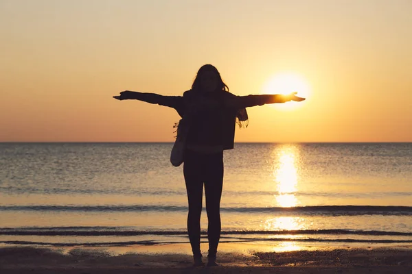 Silhouette einer Frau am Strand mit ausgestreckten Armen, untergehende Sonne auf ihrer Hand — Stockfoto