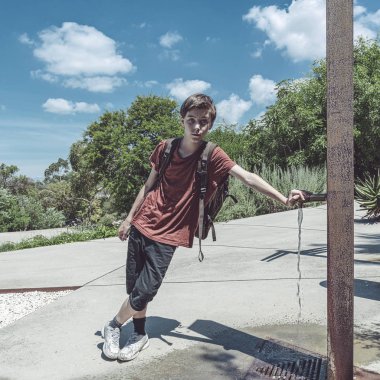 bir parkta bir musluk üzerinde sırt çantası ile genç çocuk