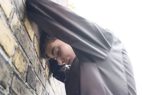 Young man standing with his head against the wall — Stock Photo, Image