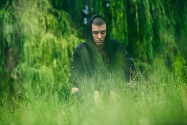 Siyah kapüşonlu üzgün çömelmiş bir adamın portresi.