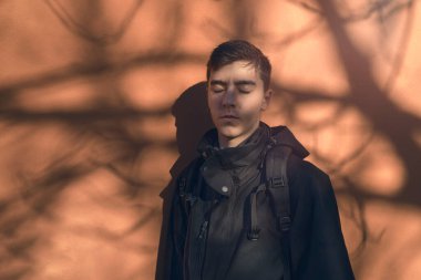 Gözleri turuncu bir duvarın önünde, gölgesi ağaç olan genç bir adamın portresi..