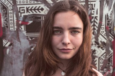 Duvarın önünde yırtık posterlerle gülümseyen genç bir kadının portresi.