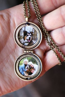 Bir kadının elini bir açık altın antika madalyon ve zincir çocuk ve bir evcil köpek içinde resimlerle tutuyor.