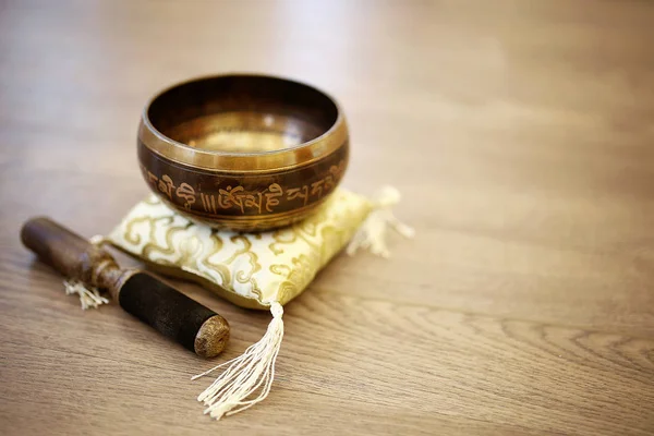 A Tibetan Singing Bowl for Yoga, relaxation, and meditation is sitting on a yellow silk pillow and on a wood background