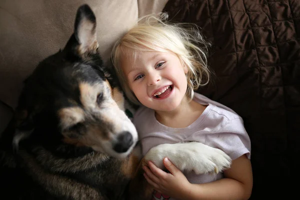 Счастливая Улыбающаяся Маленькая Девочка Обнимает Свою Собаку Пока Обнимаются Дома — стоковое фото