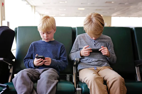 Two Children PLaying on their Cell Phones while Waiting for Airp — Stock Photo, Image