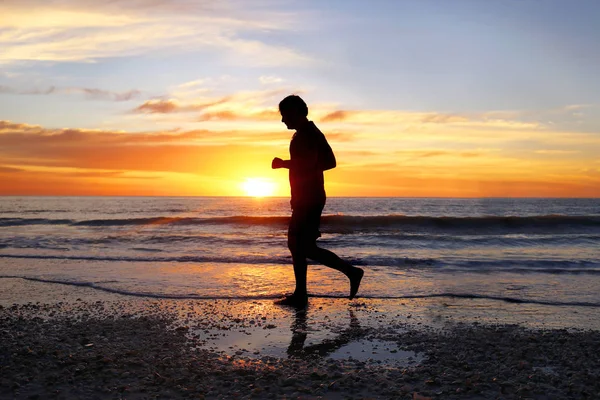 Silueta del hombre pacífico corriendo solo en la playa al atardecer —  Fotos de Stock