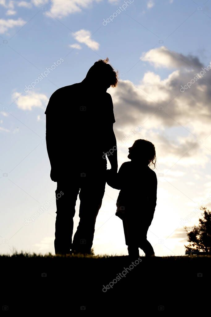 A silhouette of a sweet moment between a father and his little girld child holding hands and walking together outside at sunset.