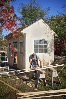 Bir marangoz küçük bir ahşap bahçe kulübesi inşa ederken tahta kesmek için dairesel testere kullanıyor..