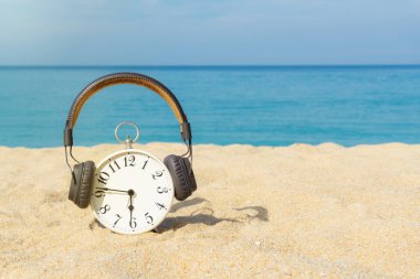 Beyaz çalar saat kahverengi kulaklıklar giyen kum üzerine yerleştirilir. Mavi deniz ve gökyüzü arka plan olarak. Gevşeme, seyahat etmek tatil ve kopya alanı ile tatil için kavram. Yaz saati.