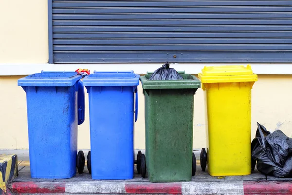 Yellow, green, blue recycling bins on public sidewalks in Phuket, Thailand. With black garbage bags placed outside