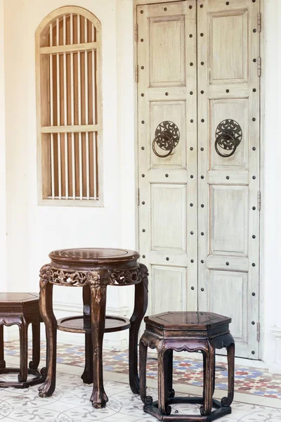 Close up antique chinese traditional chairs and table with white Chino-Portuguese door background. Asia architecture vintage style on Old Phuket Town Road, Thailand.
