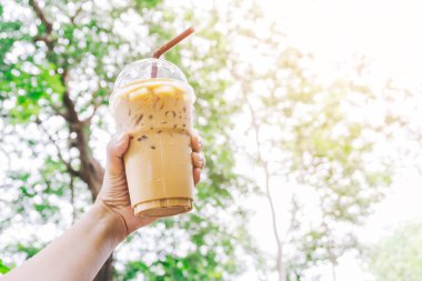 Güzel bulanık yeşil doğa arka plan üzerinde lezzetli buzlu kahve paket plastik fincan tutan genç asyalı kadın el kadar kapatın. Sağlıklı serinletici yaz içecekleri konsepti.