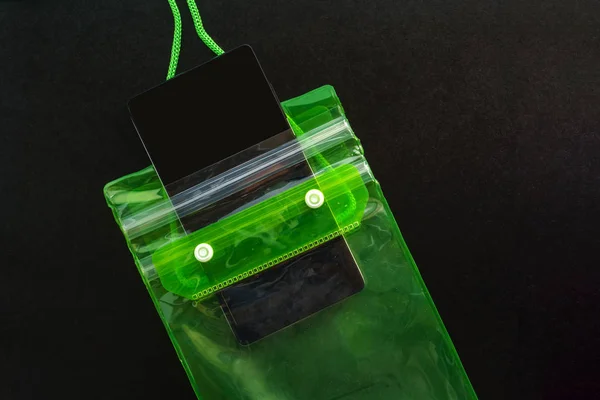 Green waterproof mobile phone case with water droplets on black texture background.PVC zip lock bag protect mobile phone or important items from water.Concept for Songkran water festival in Thailand.
