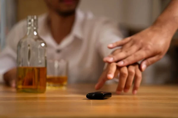 Drink no drive concept. The drunk man sitting in restaurant trying to grab the car key after he drank a lot of whiskey but his friend trying to stop him by pulling his hand out from the car key.