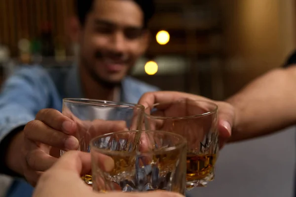 Close up shot of glasses clinking between group of friends drinking whiskey at night party in restaurant. They having so much fun drinking alcohol and talking together. Fun drinking party concept.