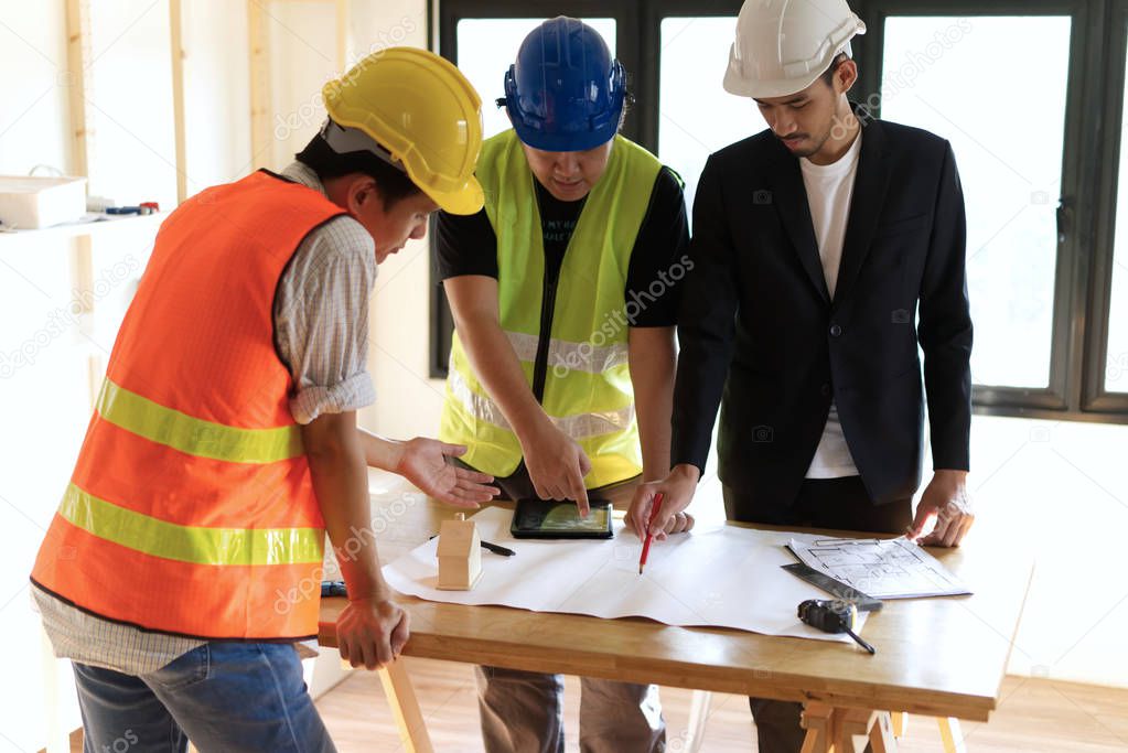 Home building members gathering on working table having some discussion for project planning. The man in suit drawing on paper while his team members giving some advice pointing finger on paper.