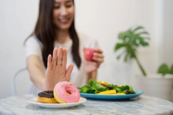 İyi bir sağlık kavramı için diyet üzerinde genç kız. Yakın el kullanarak erkek kadar onun favori donuts iterek abur cubur reddetmek ve Kırmızı elma ve salata iyi bir sağlık için seçin.