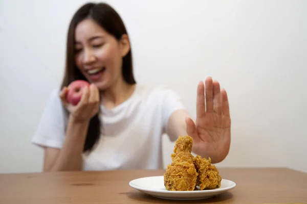 Young girl on dieting for good health concept. Close up female using hand reject junk food by pushing out her favorite fried chicken and choose red apple and salad for good health.