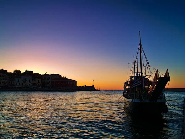 Girit adası Yunanistan'da Chania limanında gün batımı. Alacakaranlıkta canlı canlı renkler. Ön planda yelkenli gemi teknesi.