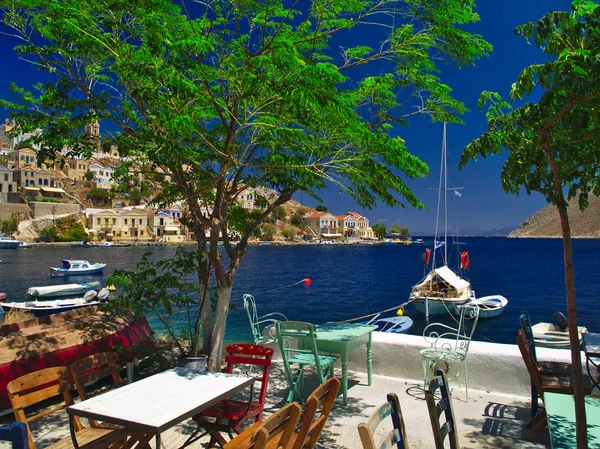 ギリシャのシミ島からの夏のショット テーブルチェアボートクリスタルクリアな海と多色の家とカフェからの眺め — ストック写真
