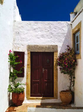 Kahverengi ahşap kapı, çiçek ve derin mavi yaz gökyüzü ile seramik kaplar ile güzel beyaz ev. Patmos island, Yunanistan