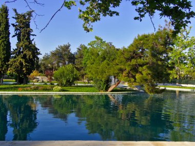 Bir parkın içindeki göl. Göldeki küçük bir ada ve ona giden köprü. Çam selvi ve çınar ağaçları. Alsos Filadelfeias, Atina, Yunanistan.
