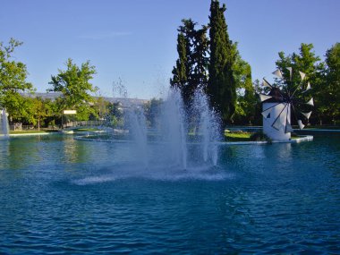 Bir park gölü içinde, küçük bir adada Çeşme ve güzel yel değirmeni. Ayrıca Filadelfeias, Atina, Yunanistan. Berrak bahar günü.