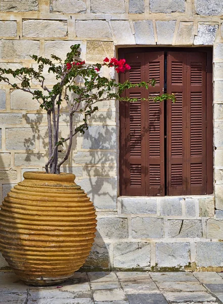 Ceramic jar pot with bougainvillea and wooden window against traditional stone wall, Tinos island, Greece.
