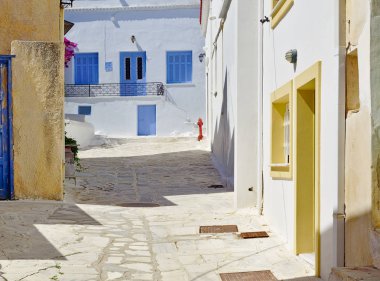 Güzel huzurlu taş döşeli boş sokak, öğle vakti mavi ve sarı pencereler ile beyaz evler ve yangın hidrant Tinos ada, Yunanistan.