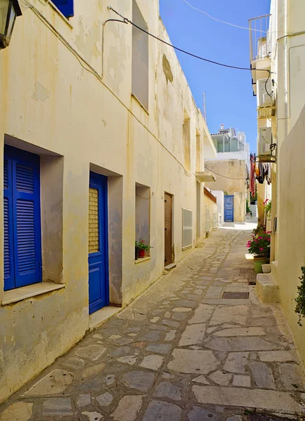 Güzel huzurlu taş öğle vakti mavi pencereli beyaz evler ile boş sokak döşeli, Tinos adası, Yunanistan.