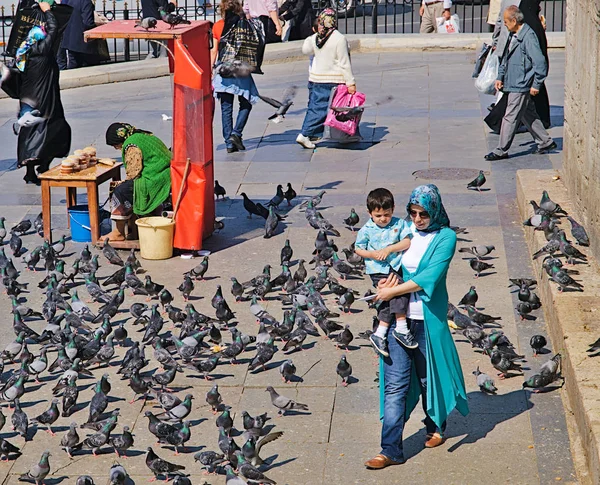 İstanbul, Türkiye - 24.05.2010: Eminönü ilçesinde, çocuk taşıyan genç kadın, kuşlar ve çok sayıda güvercin için yiyecek satan yaşlı kadın büfesi.