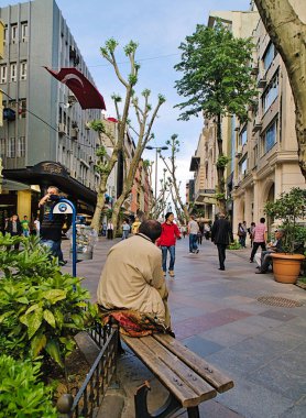  Bir adamın arkası, birçok mağaza ve alışverişçiyle işlek bir sokaktaki bankta oturuyor..