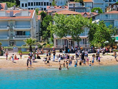 İstanbul, Türkiye - 28.05.2010: İnsanlar turkuaz sulu bir plajda denizin tadını çıkarıyor. İstanbul Boğazı'nda seyir halindeki bir gemiden görünüm.